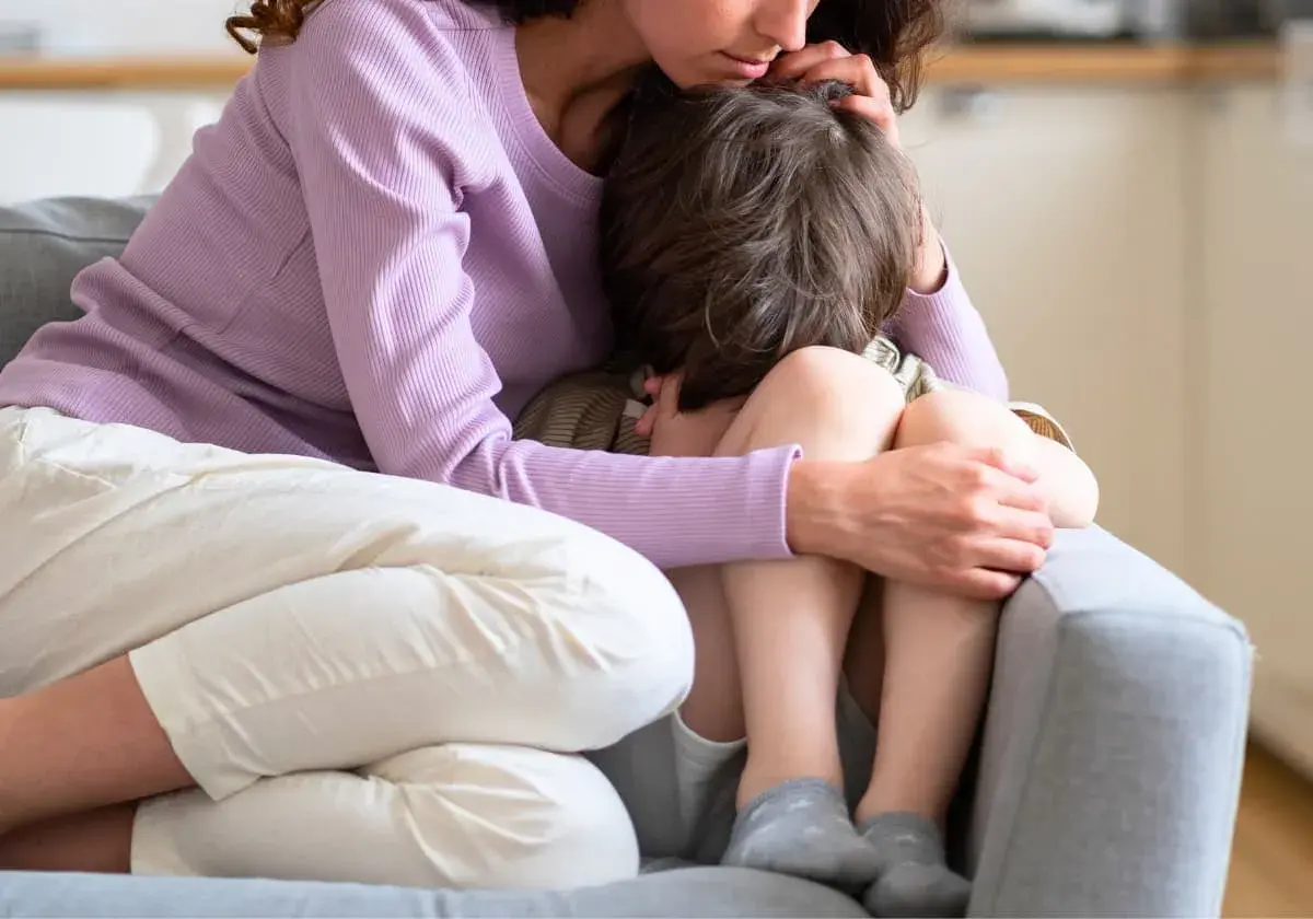 En mamma tröstar sitt barn som kramar sina knän. Barnet verkar oroligt, kanske upplever separationsångest.