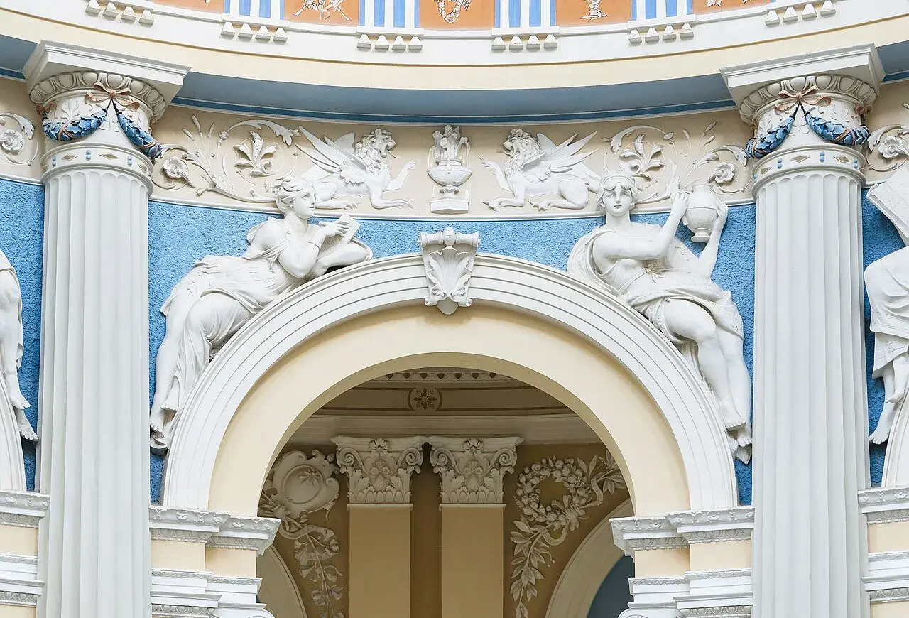 Barokowe stiuki: rzeźby kobiet, gryfy i ornamenty na tle błękitnej ściany.