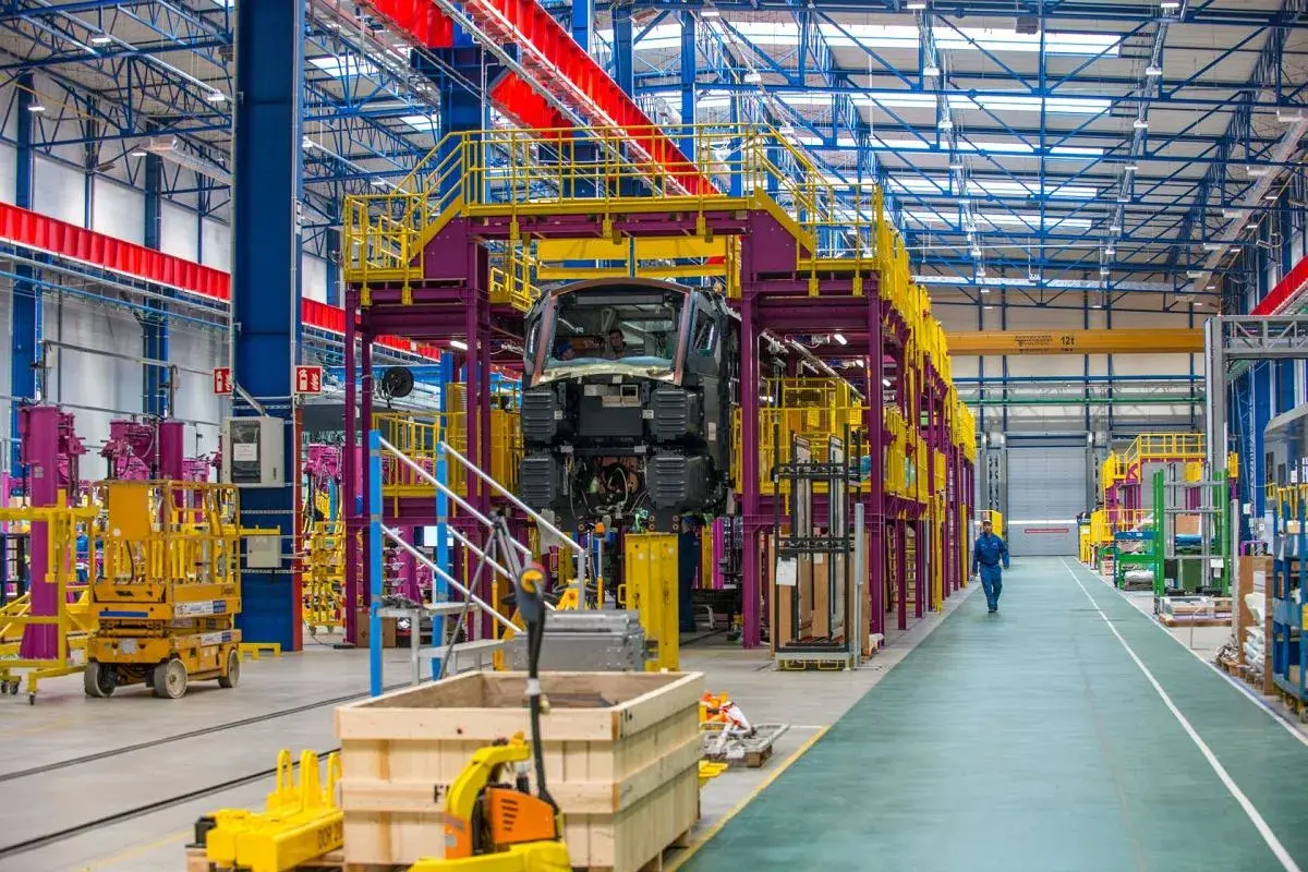 W hali produkcyjnej Alstom Konstal powstaje nowoczesny pociąg. Widać fragmenty konstrukcji, podnośniki i pracownika w niebieskim kombinezonie.