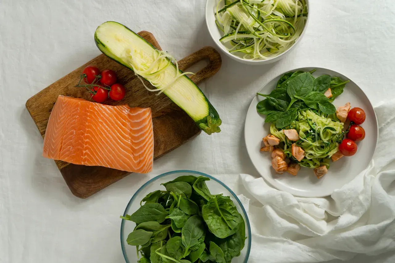 Składniki na dietę low carb przepisy: surowy łosoś, cukinia spiralizowana, pomidorki koktajlowe i świeży szpinak.