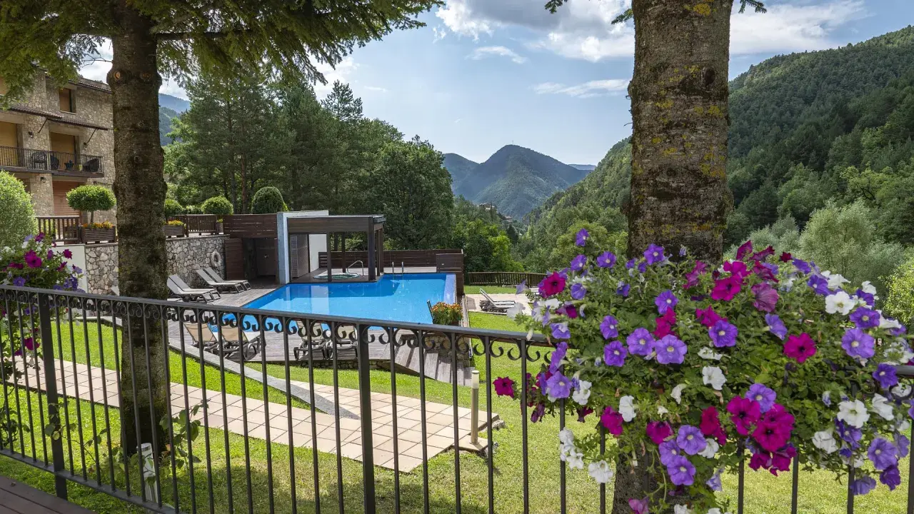 Un hotel de montaña con piscina azul, rodeado de vegetación. La coma i la pedra, un lugar de ensueño.