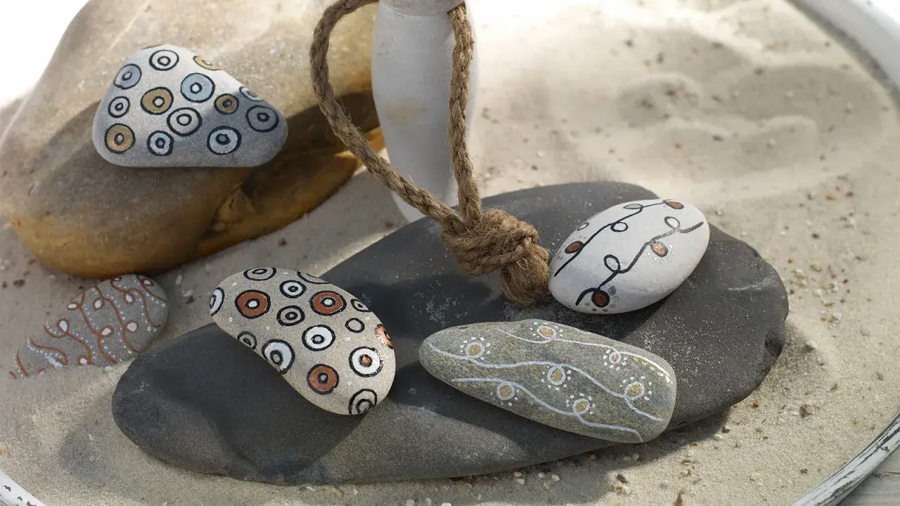 Ideas para pintar piedras de playa: piedras decoradas con círculos concéntricos y líneas onduladas en tonos tierra y blanco.
