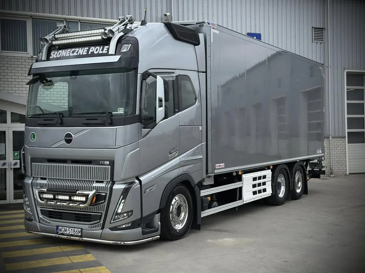 Srebrny Volvo FH16 z naczepą chłodniczą, ozdobiony dodatkowymi światłami i napisem "Słoneczne Pole".