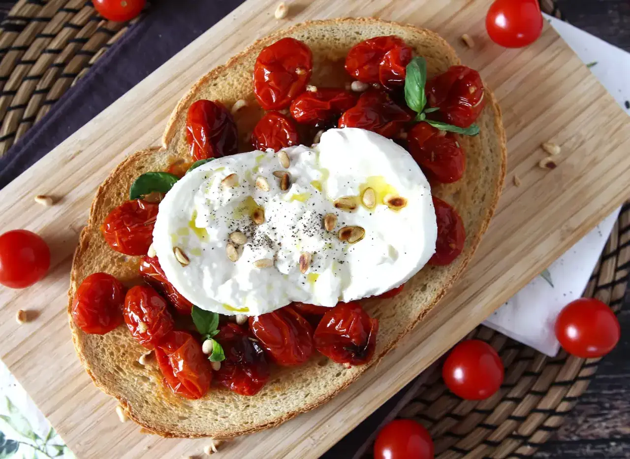 Pyszna bruschetta z burratą, pieczonymi pomidorkami koktajlowymi i orzeszkami pinii. Idealna na lekki posiłek.