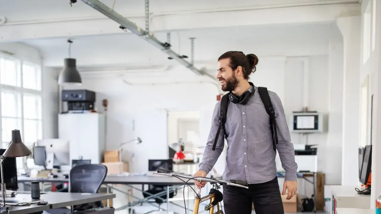 Junger Mann mit Fahrrad und Rucksack im Büro, bereit für sein online studium in Berlin.