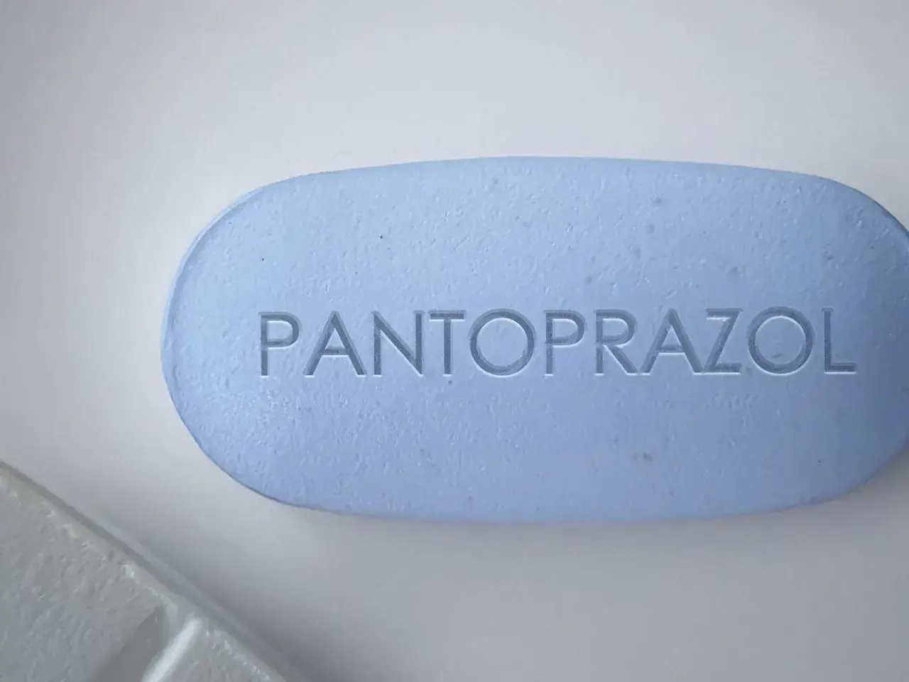 Ein hellblaues Pantoprazol-Tablett mit eingeprägtem Schriftzug. Manche Menschen nehmen Pantoprazol und Magnesium zusammen ein.