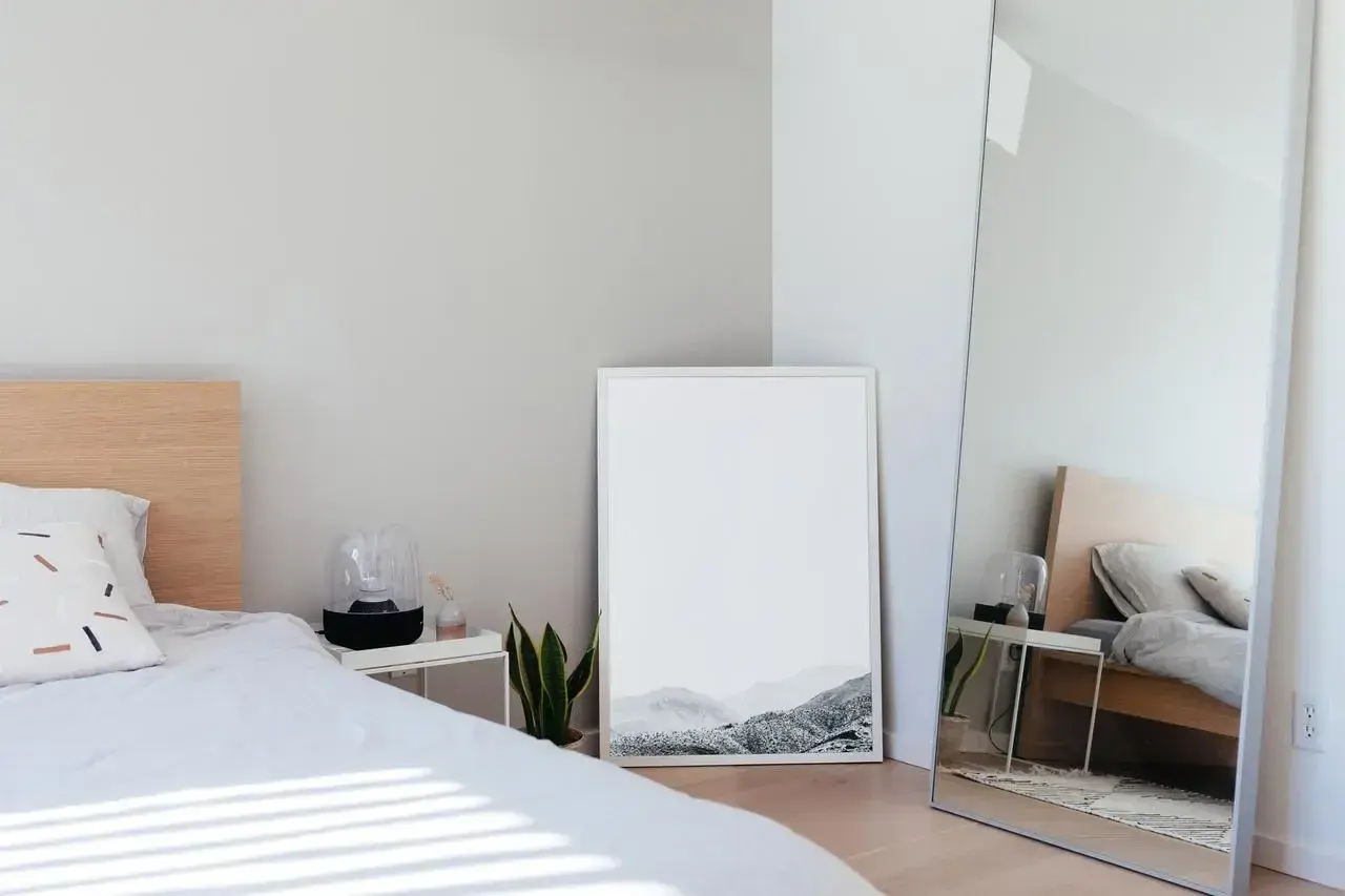 Jasne, minimalistyczne lustro w sypialni feng shui odbija łóżko i tworzy wrażenie większej przestrzeni.