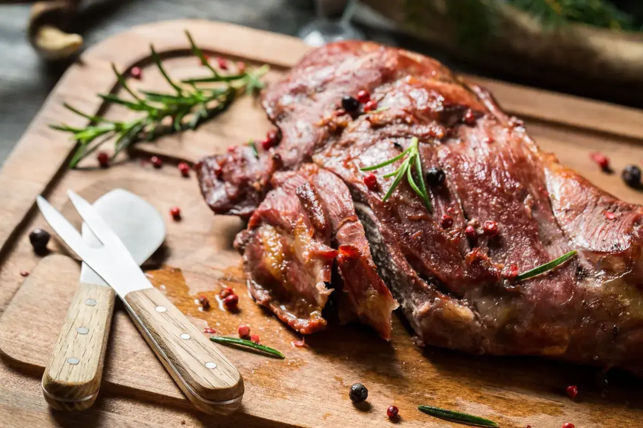 Soczysta dziczyzna, pieczona z rozmarynem i pieprzem, czeka na desce do krojenia. Obok leżą sztućce do mięsa.