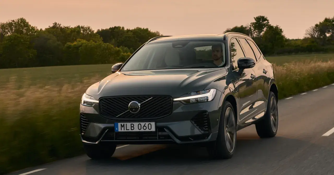 Ciemnoszary Volvo XC60 2025 jedzie drogą wśród zieleni o zachodzie słońca.