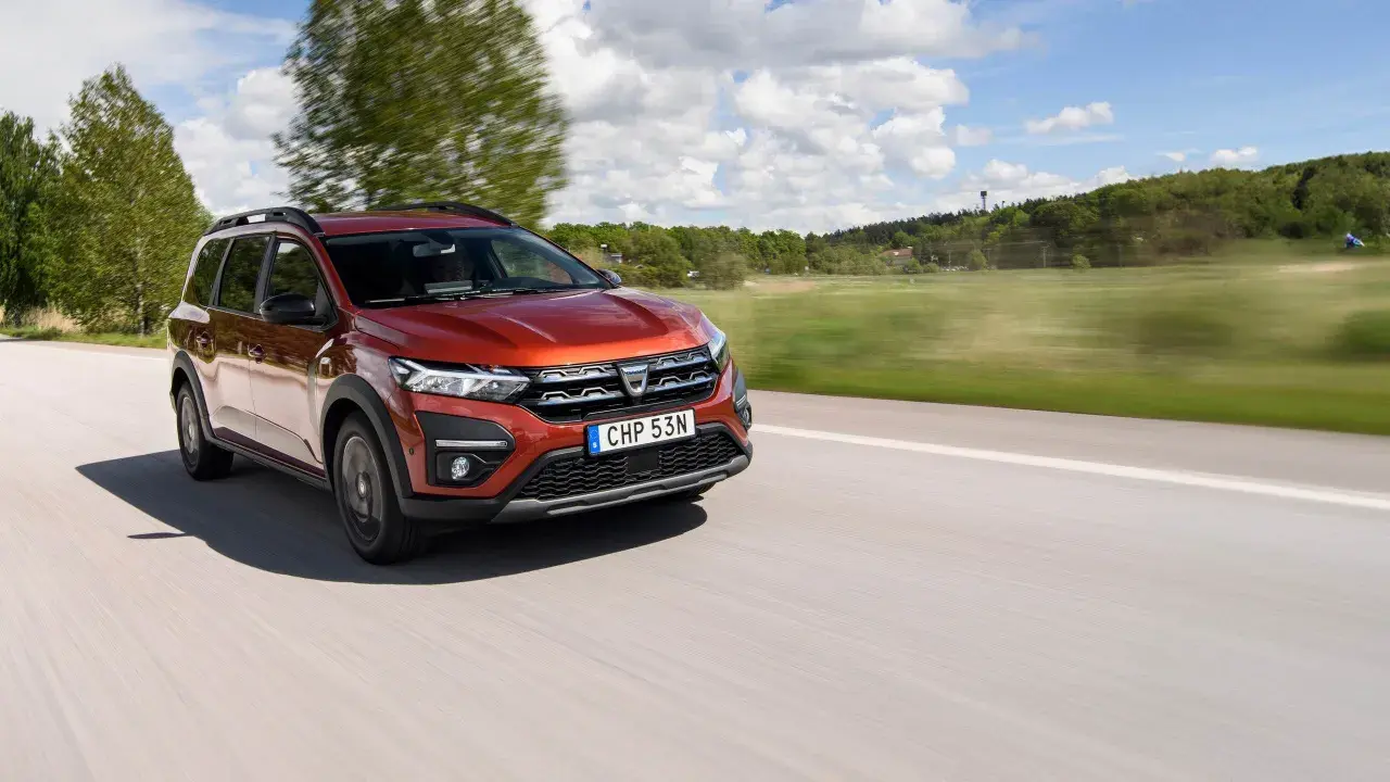 En röd Dacia Jogger begagnad kör på en landsväg i Sverige. Bilen är i rörelse med suddig bakgrund.