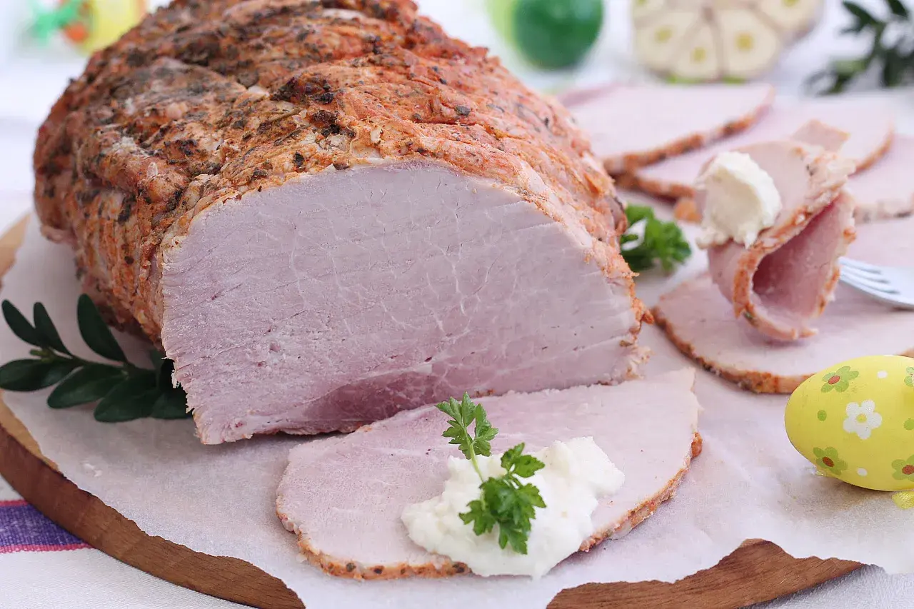 Soczysta szynka pieczona w rękawie, pokrojona w plastry, z chrzanem i natką pietruszki. Idealna na wielkanocny stół.