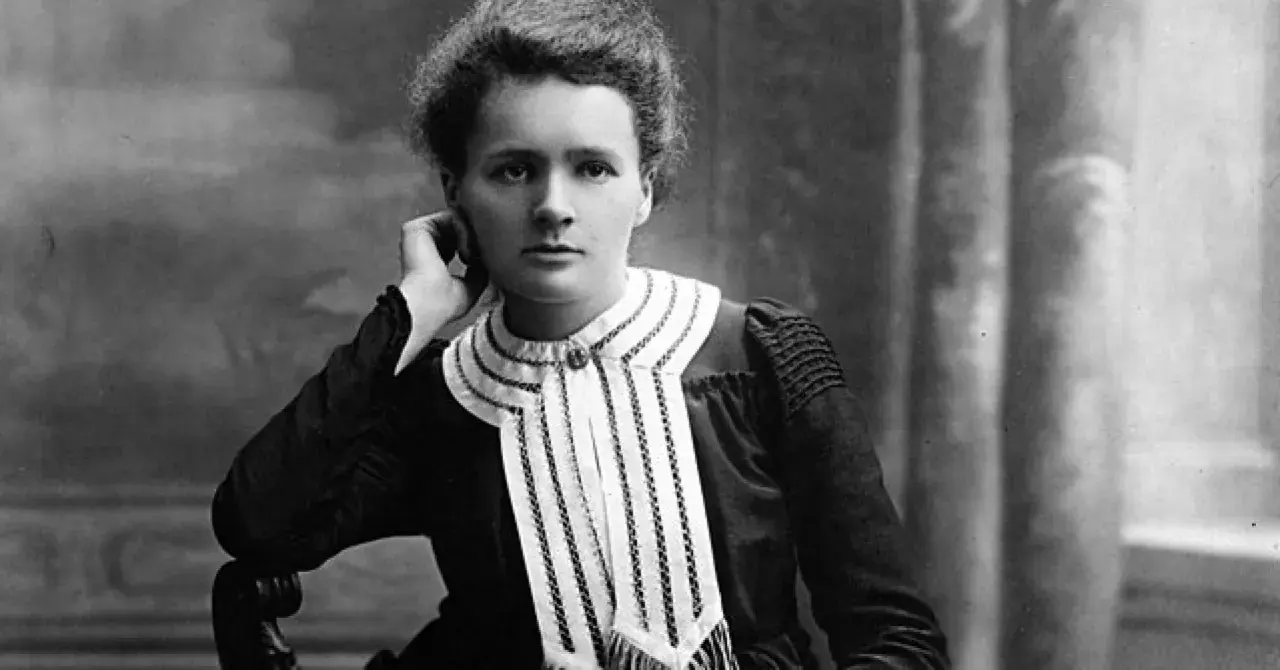 Czarno-białe zdjęcie Marii Skłodowskiej-Curie w eleganckiej sukni z ozdobnym kołnierzem.