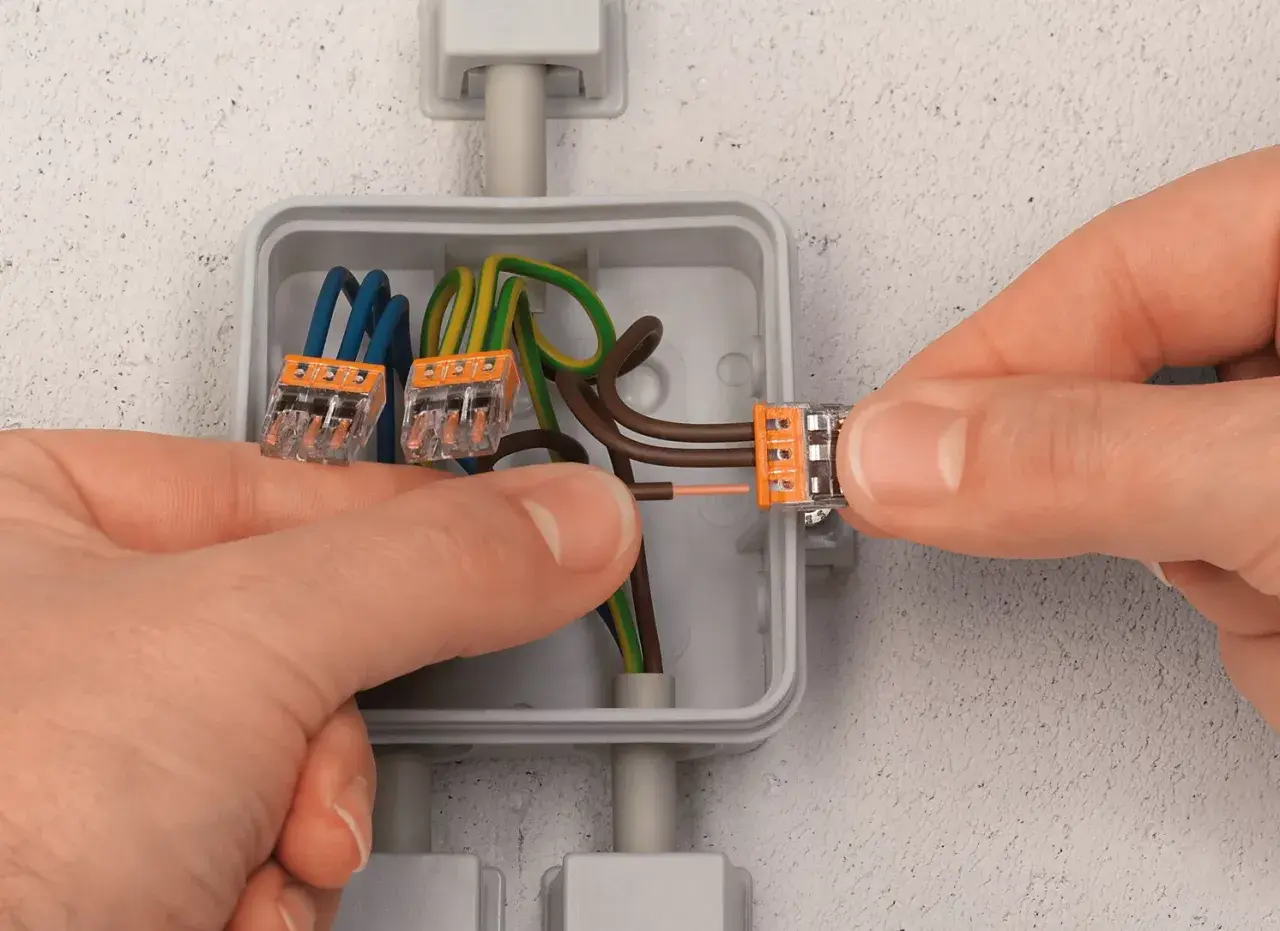 Mains électriques connectées dans une boîte encastrée. Le diamètre de la boîte encastrement permet d'accueillir les fils et les connecteurs.
