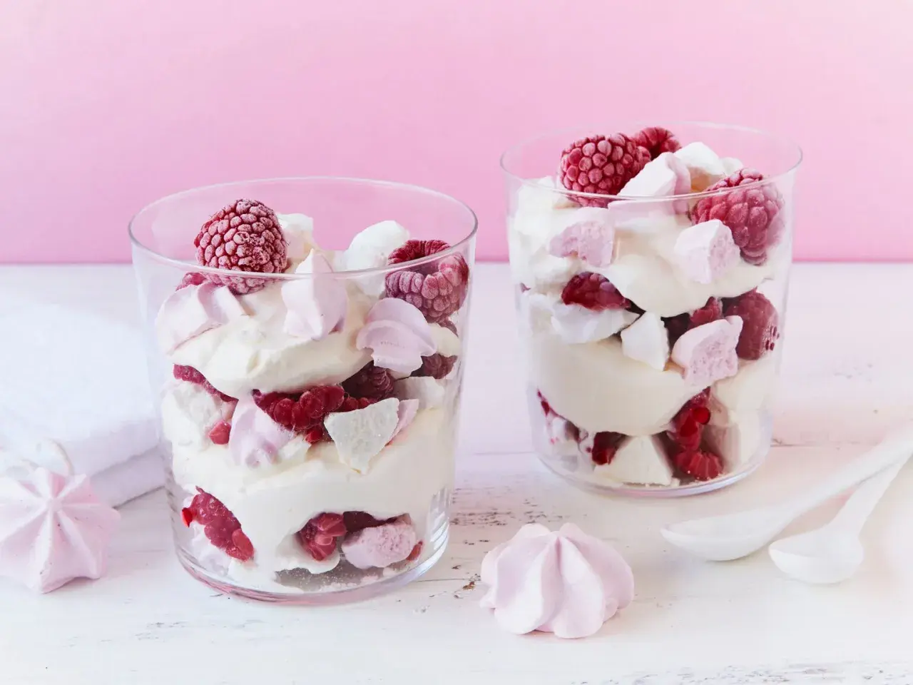 Zwei Gläser mit Himbeer Baiser Dessert, geschichtet mit Sahne, frischen Himbeeren und zarten Baiserstückchen.