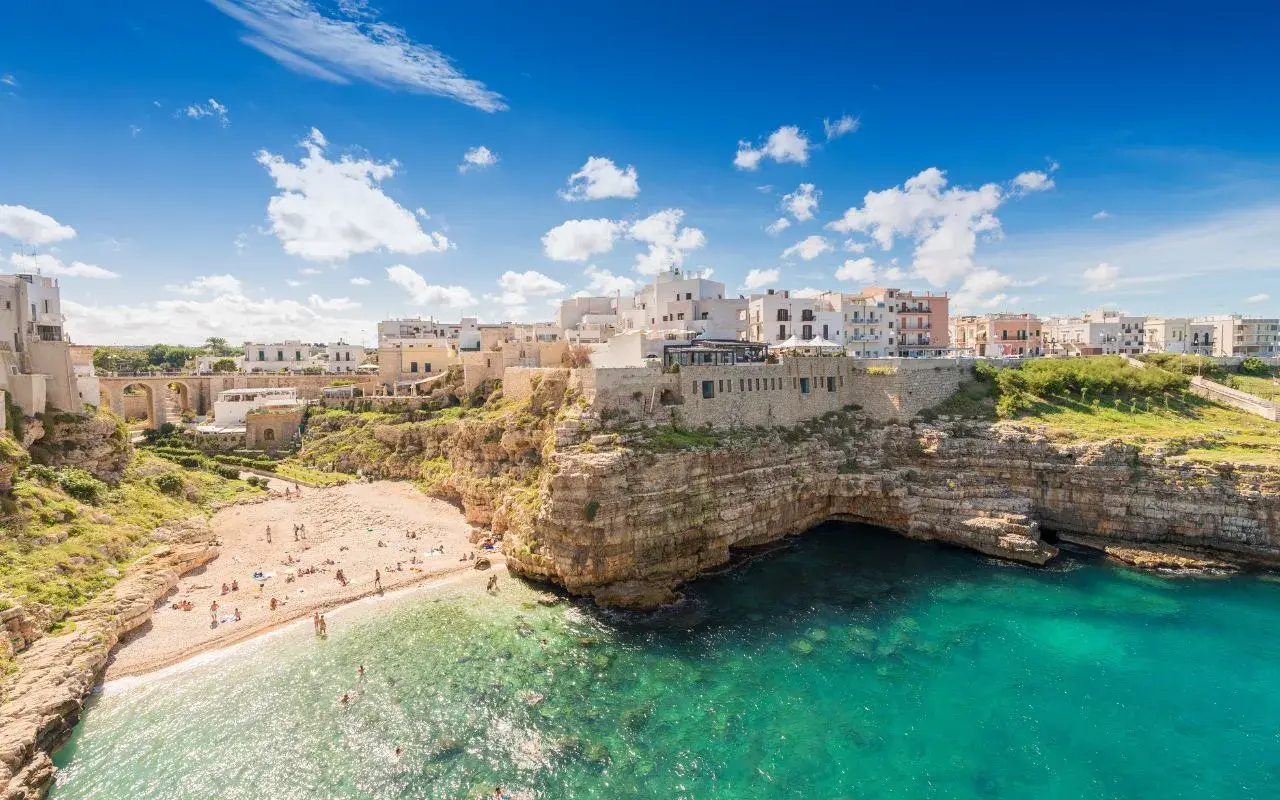 Vue panoramique de la plage de Polignano a Mare, avec ses falaises rocheuses, ses eaux turquoise et ses maisons blanches perchées.