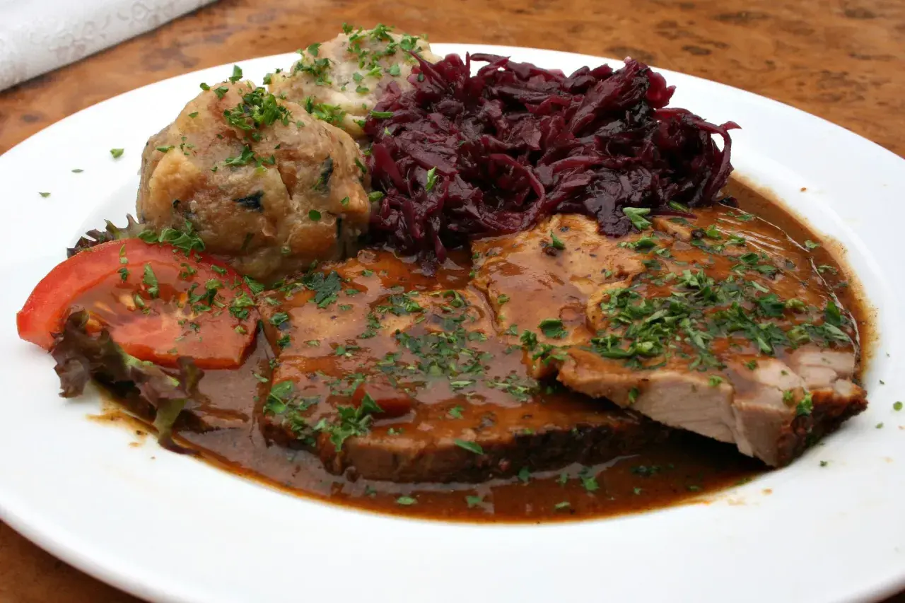 Pyszne jedzenie w Niemczech: pieczeń wieprzowa w sosie, kluski ziemniaczane, czerwona kapusta i pomidor.