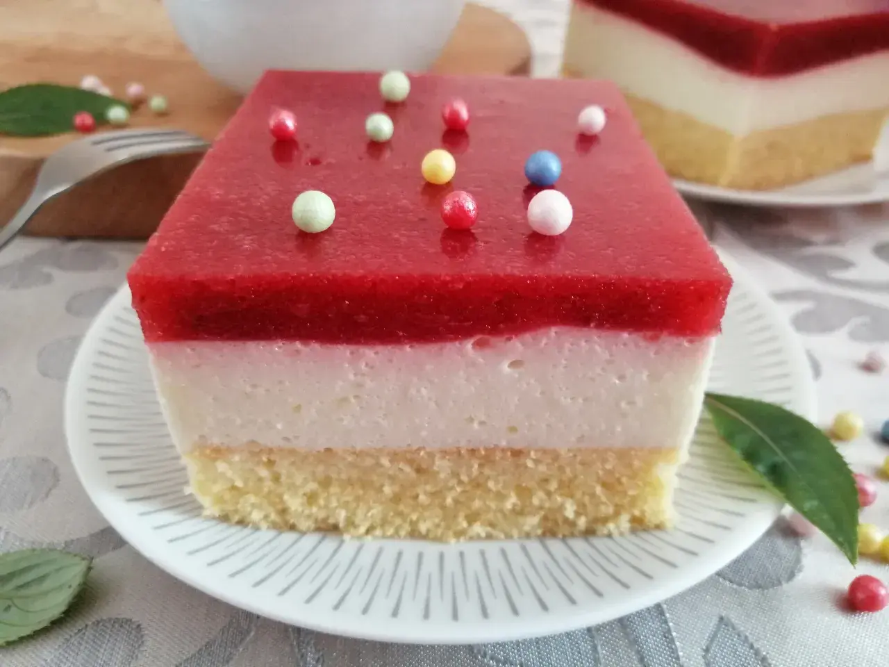 Pyszna żelka truskawkowa z mrożonych truskawek, z kremową warstwą i biszkoptem, ozdobiona kolorowymi kuleczkami.