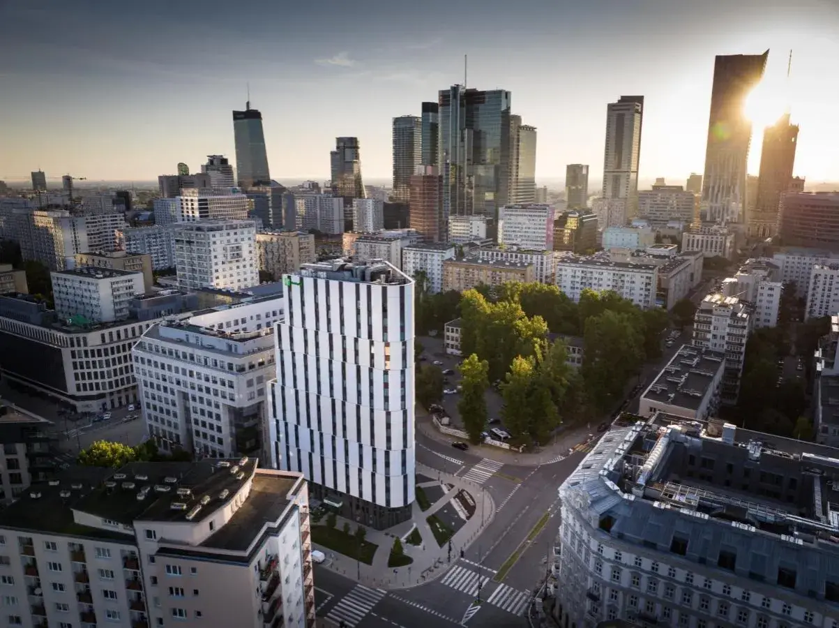 Widok na miasto z nowoczesnym budynkiem Holiday Inn Twarda w centrum. W tle wieżowce i zieleń.