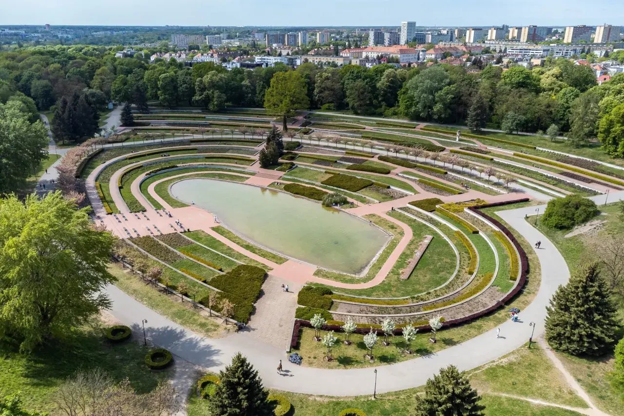 Widok z lotu ptaka na park Cytadela z jeziorem, tarasami i alejkami. W tle zabudowania miejskie.