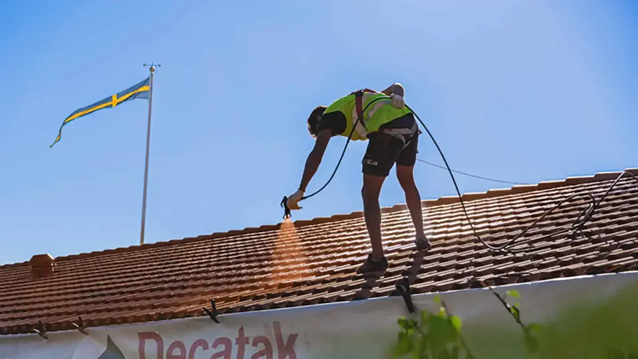 Arbetare sprutmålar tak med svensk flagga i bakgrunden.