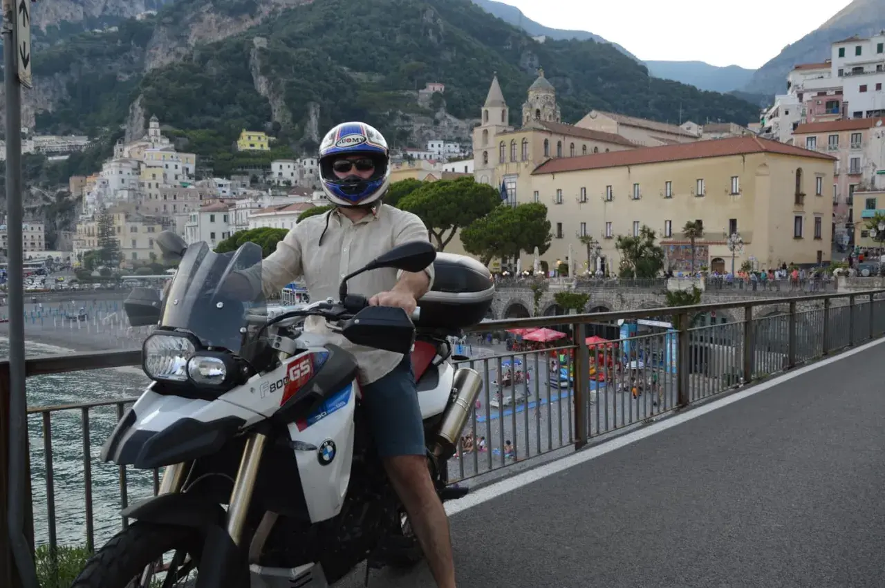 Motociclista in sella alla sua BMW, ammira il panorama della meta costiera amalfitana con le case aggrappate alla montagna.