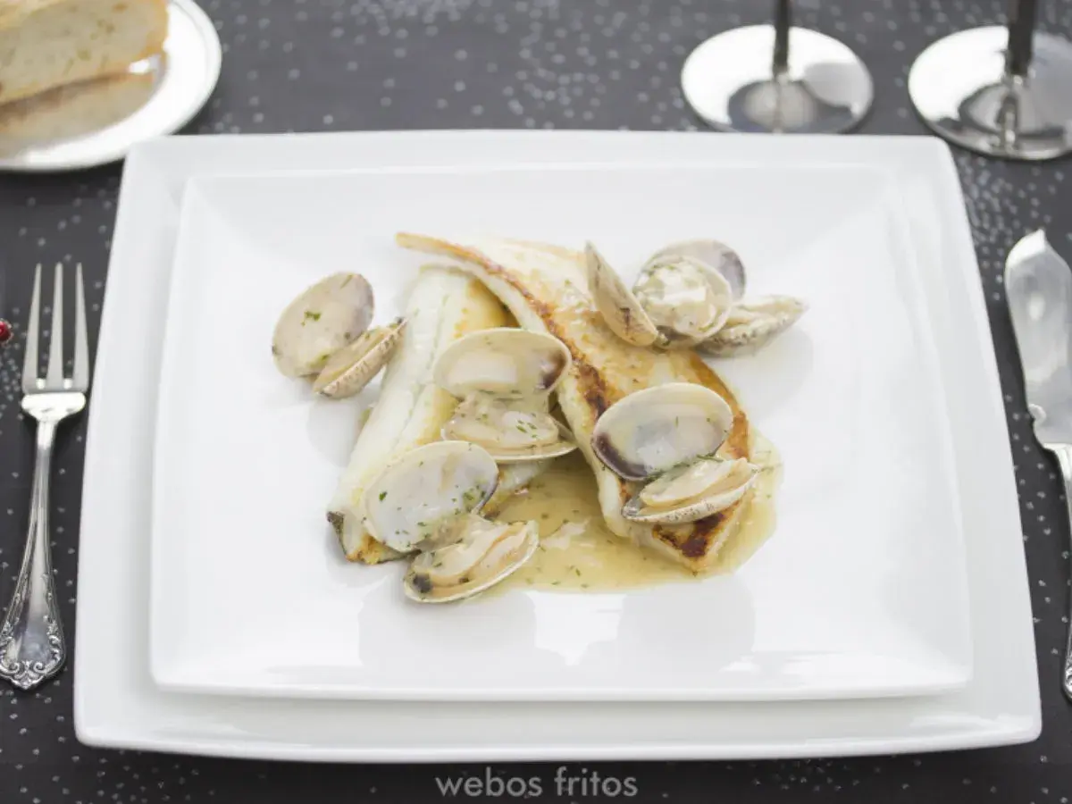 Coruxo pescado con almejas en salsa cremosa, servido en plato blanco.