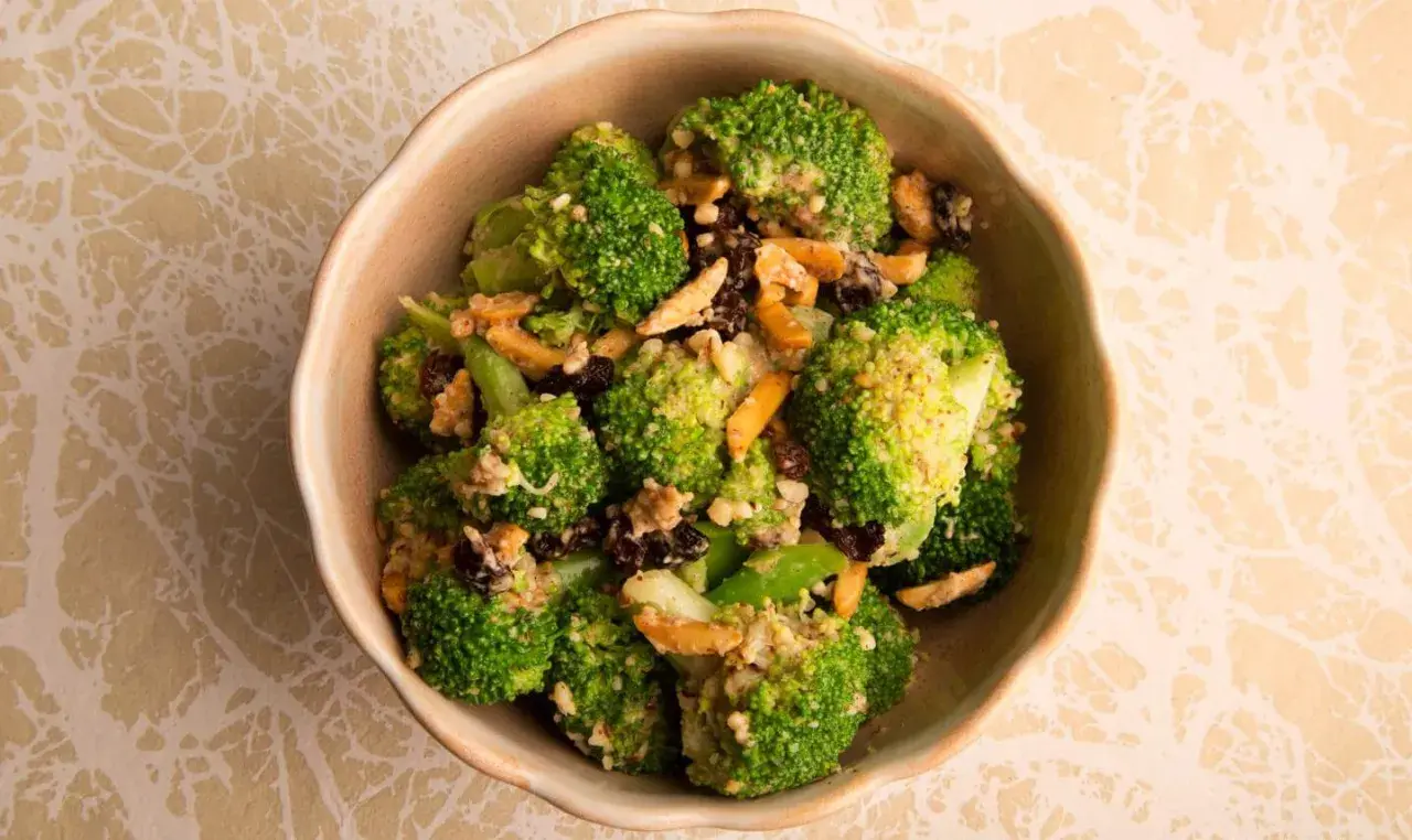Ensalada de brócoli fresca con pasas y nueces, servida en un cuenco de cerámica.