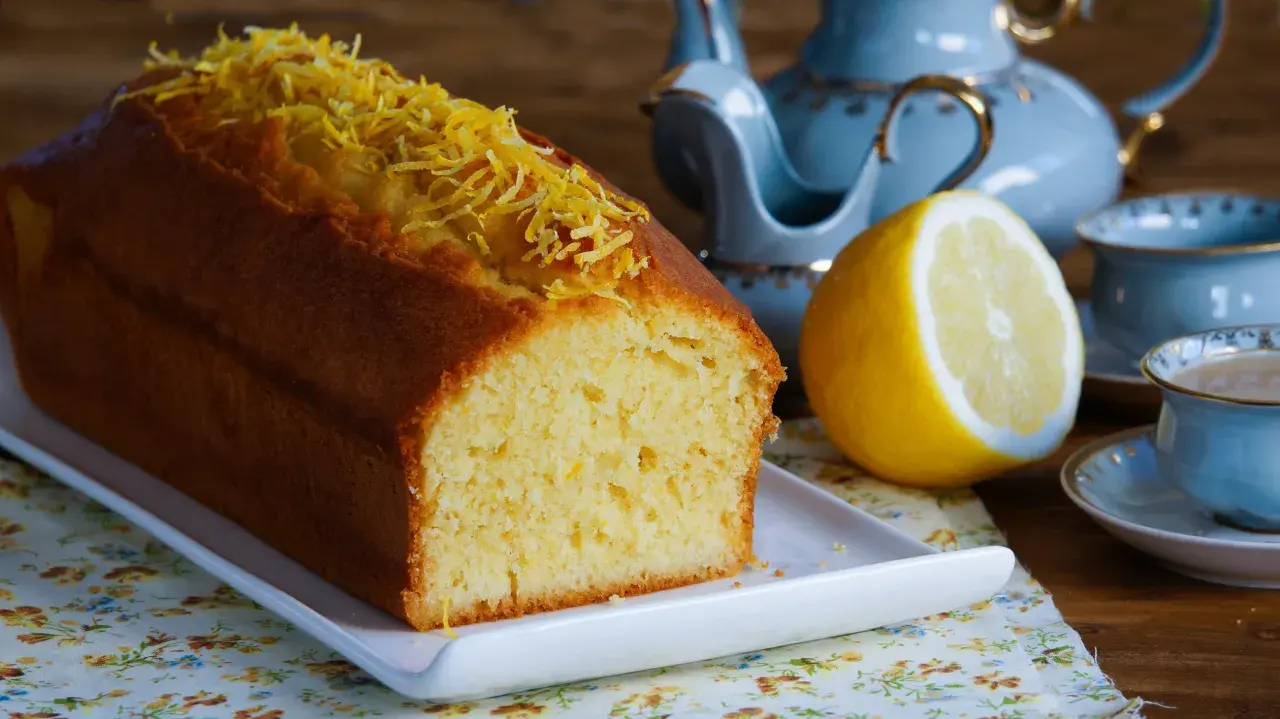 Puszysta babka cytrynowa, ozdobiona skórką cytrynową, czeka na herbatę z błękitnego serwisu.