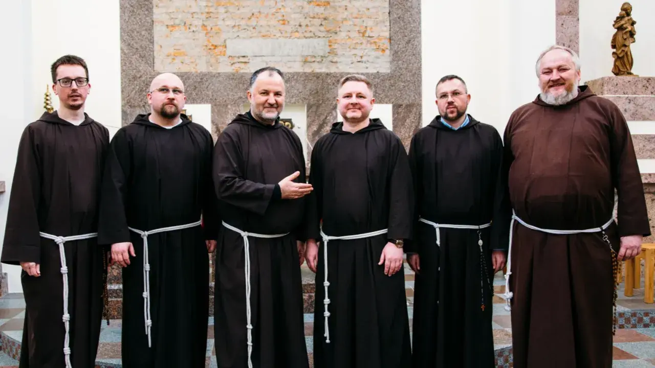 Sześciu mężczyzn w brązowych habitach, każdy z białym sznurem przepasanym w pasie. To grupa kapucynów.