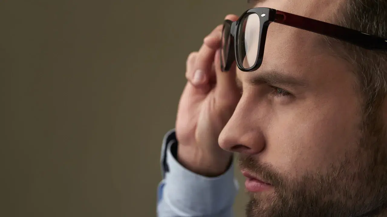 Mężczyzna z dużą wadą wzroku poprawia okulary.