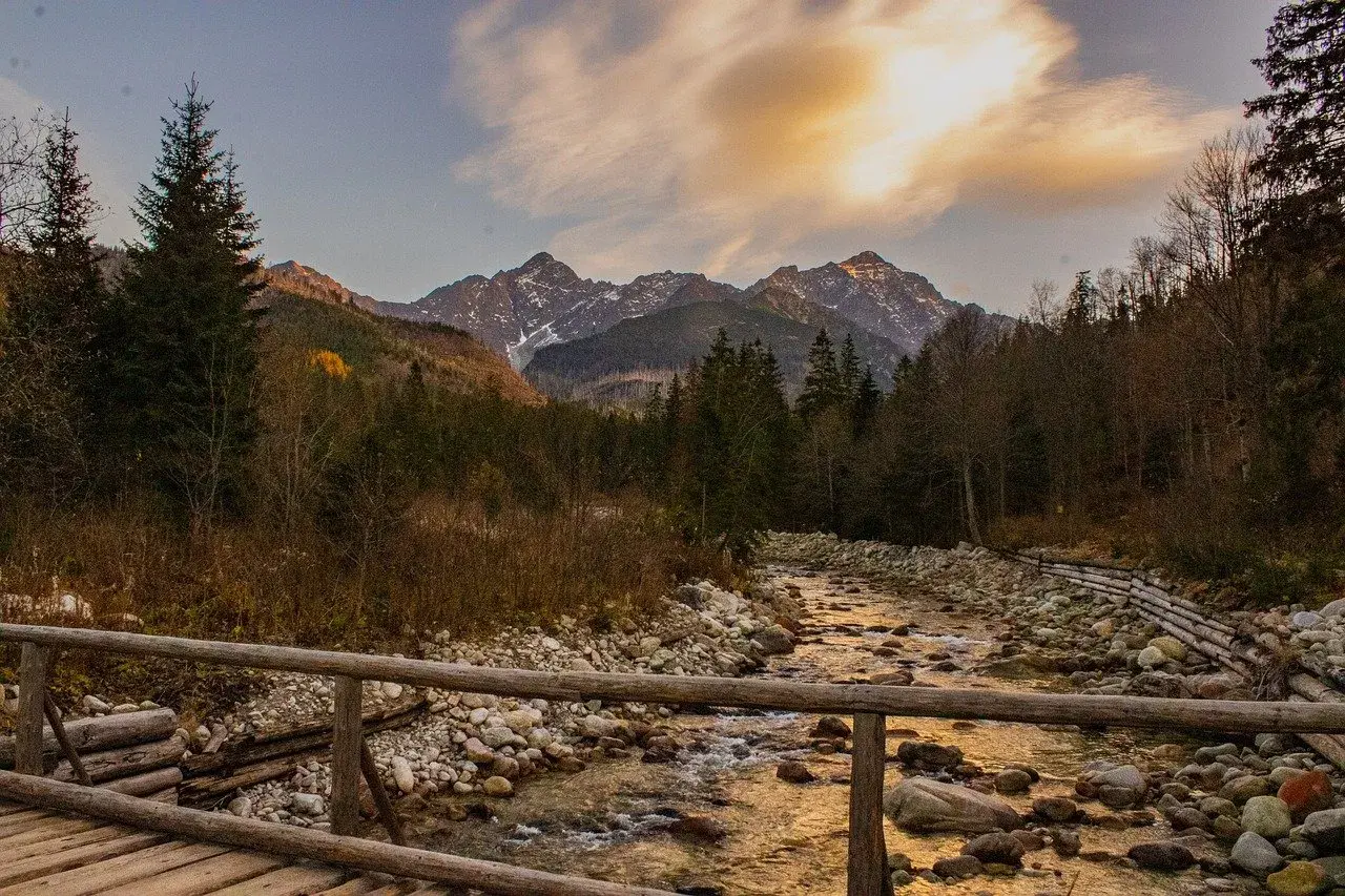 Jesienne Tatry w październiku. Drewniany mostek nad kamienistym potokiem, w tle góry i lasy.