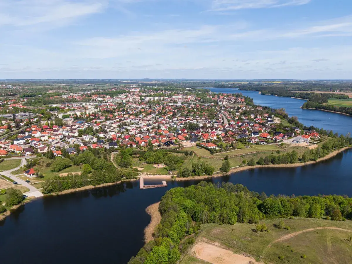Widok z lotu ptaka na miasteczko nad jeziorem, jedno z największych rynków w Polsce, z domami z czerwonymi dachami i zielenią.