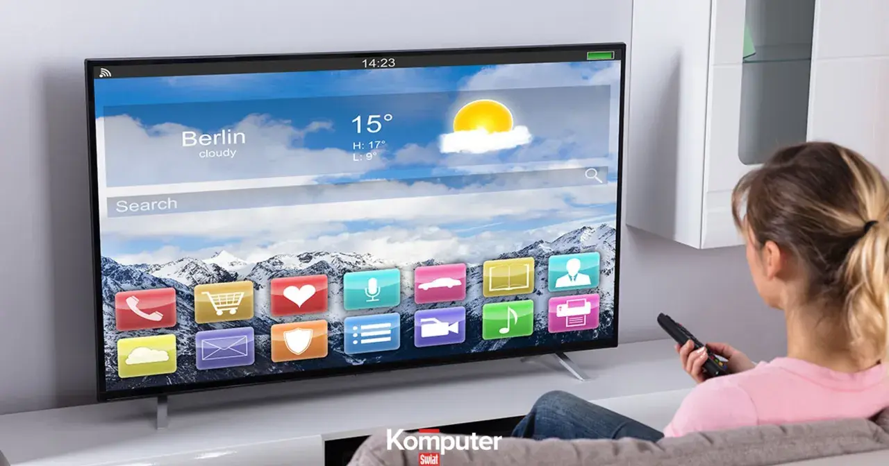 Kobieta z pilotem ogląda nowoczesny telewizor LCD, na którym wyświetla się interfejs z ikonami aplikacji i prognozą pogody dla Berlina.