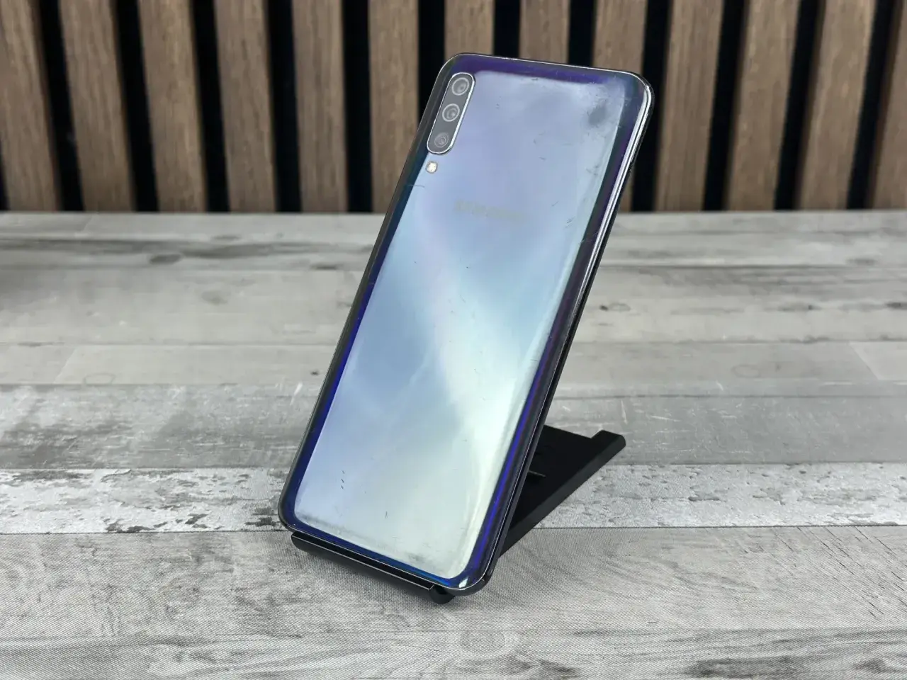 Telefon Samsung Galaxy A50 na czarnym stojaku, z widocznym logo Samsung. Sprawdź aktualną samsung galaxy a50 cena.