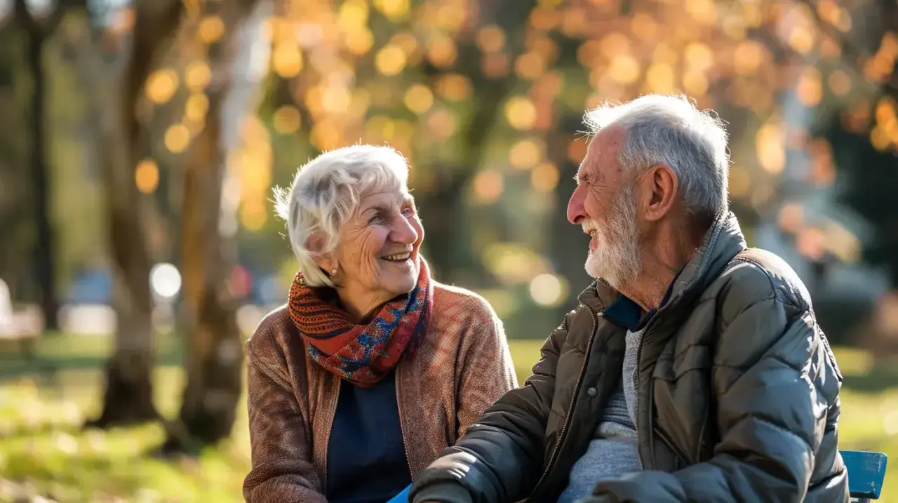 Uśmiechnięta para seniorów cieszy się jesiennym dniem w parku. Dobre samopoczucie zawdzięczają pewnie zdrowej diecie i codziennej multiwitaminie.