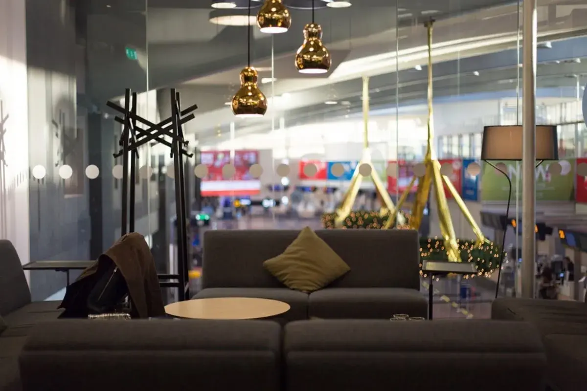 Mysig lounge med soffor, bord och lampor. En jacka hänger på en klädhängare. Utsikt över flygplatsen från Pearl Lounge Arlanda.