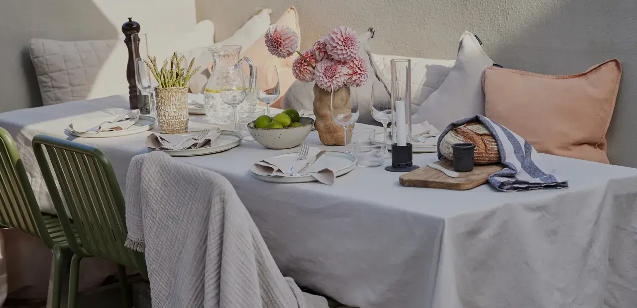 En vacker dukning utomhus med blommor, ljus och nybakat bröd. En inbjudande scen för en somrig middag.