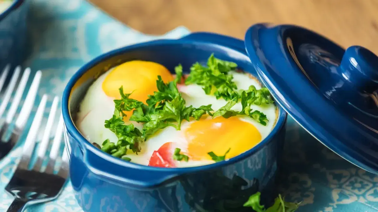 Un délicieux oeuf cocotte, deux jaunes d'œufs brillants dans leur ramequin bleu, parsemé de persil frais. Prêt à être dégusté !
