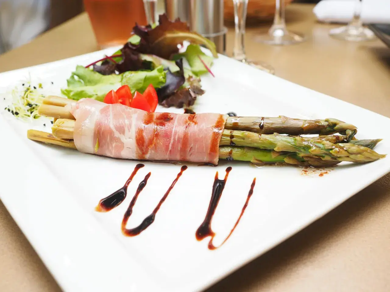 Zielone szparagi owinięte szynką parmeńską, podane z sałatką i sosem balsamicznym.