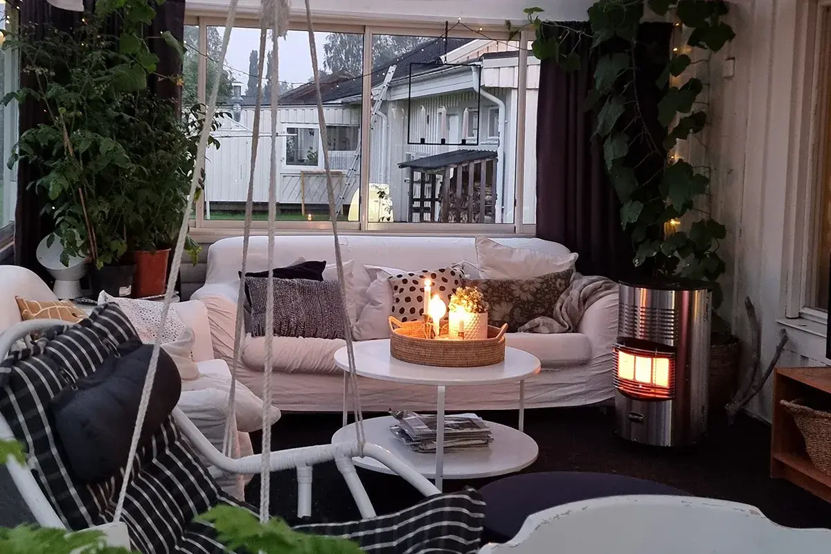 Mysig stuga inredning med soffa, korgstol, växter och tända ljus. En gasolkamin ger värme.