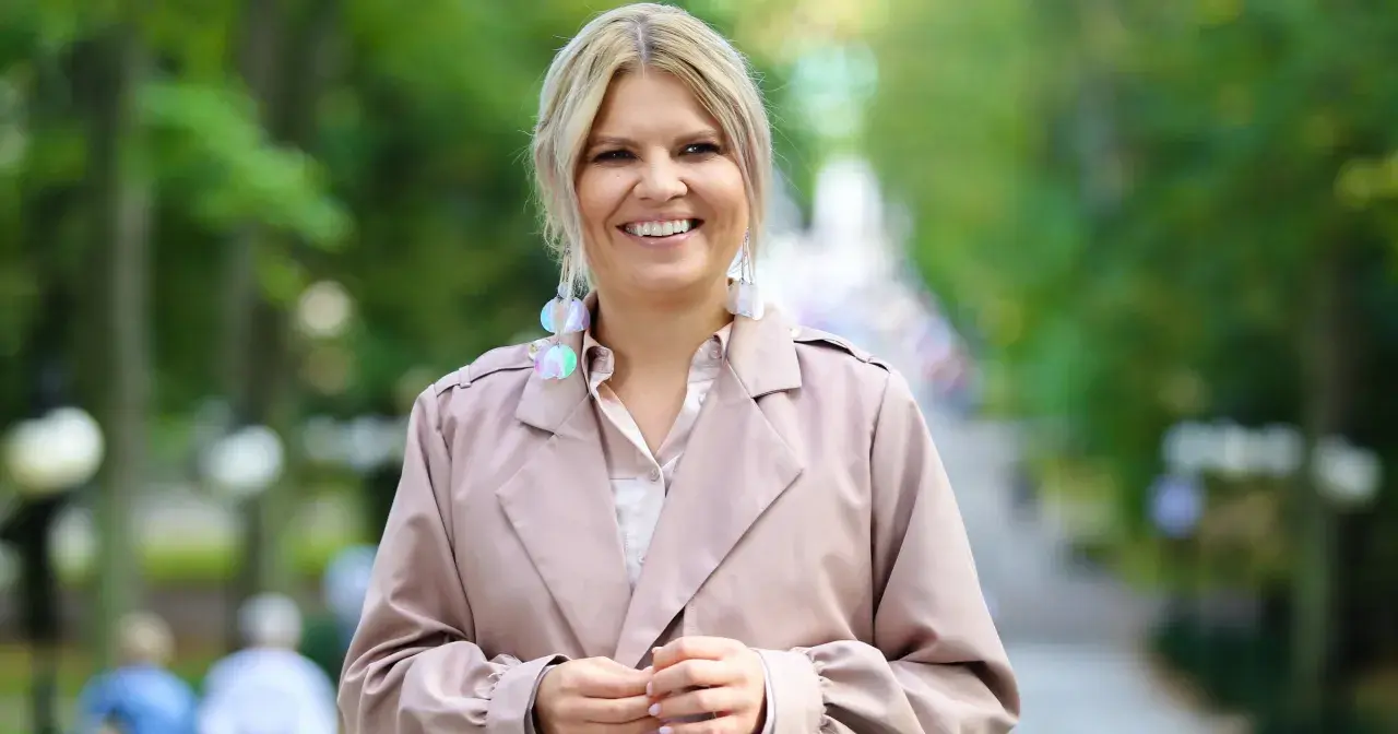 Uśmiechnięta Marta Manowska w beżowym płaszczu i efektownych kolczykach, jakby właśnie spotkała swojego partnera.