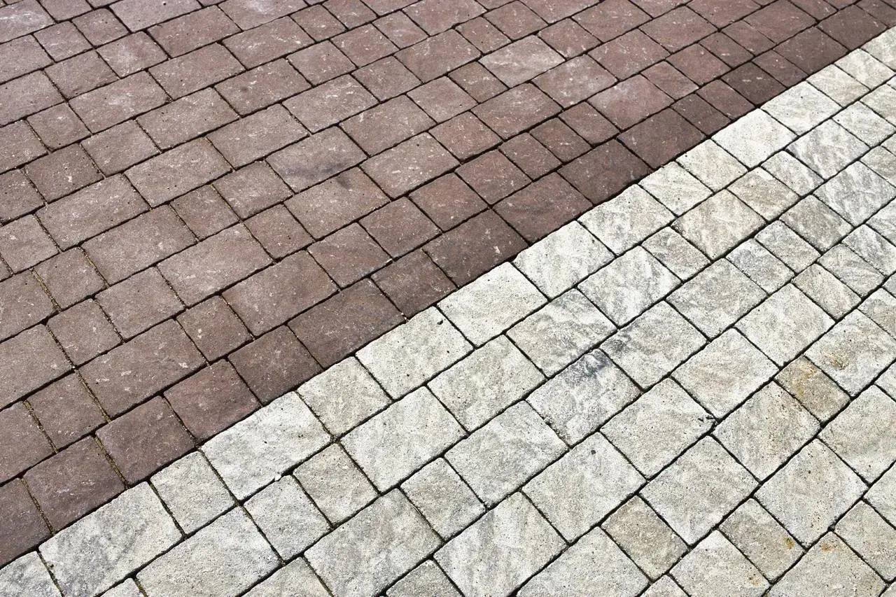 Pavimentazione esterna con blocchi di cemento color tortora e grigio chiaro, disposti a spina di pesce.