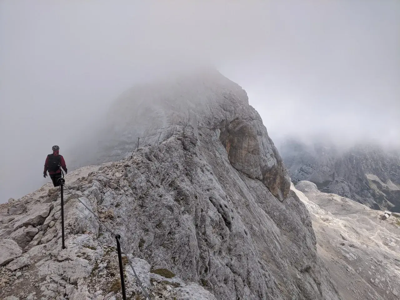 Turysta na skalistej ścieżce, wspinający się po via ferracie. Mgła otula szczyty, tworząc mistyczną atmosferę na szlakach Triglavu.