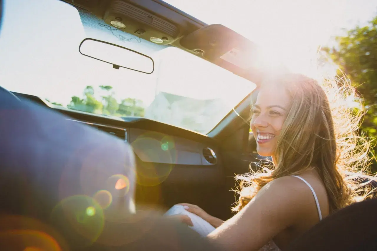 Vrolijke vrouw in cabriolet, haar haar wappert in de zon. Ze lacht, niet te streng voor jezelf, genietend van de rit.
