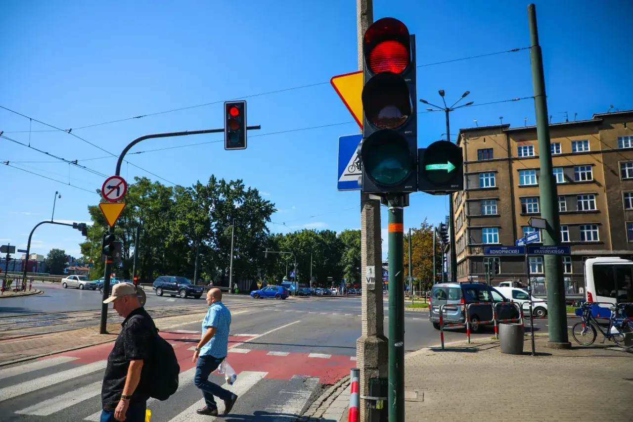 Sygnalizator S2 z zieloną strzałką w prawo, czerwonym światłem u góry. Ludzie przechodzą przez pasy.