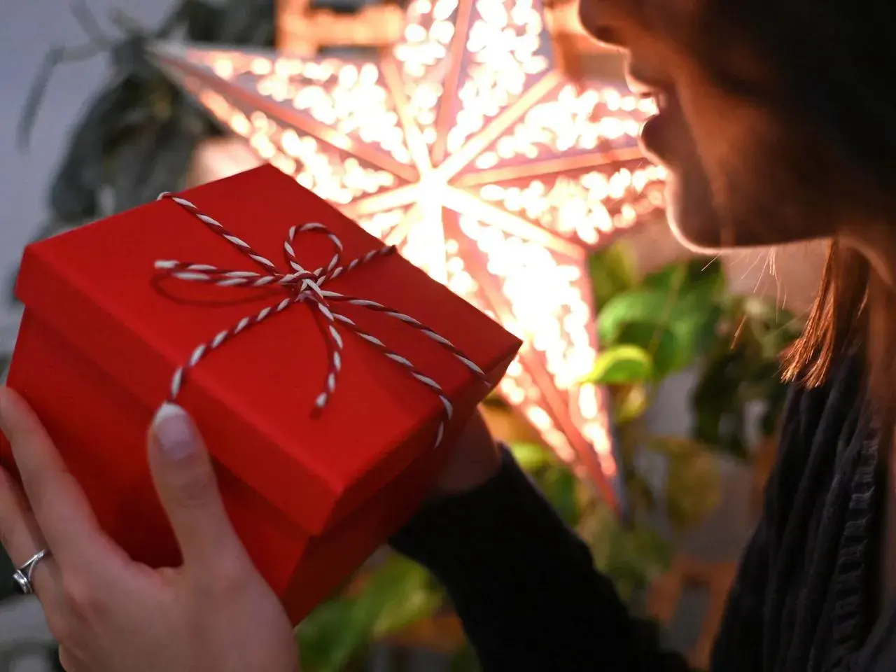 Ein rotes Weihnachtsgeschenk in Händen, im Hintergrund ein leuchtender Stern.