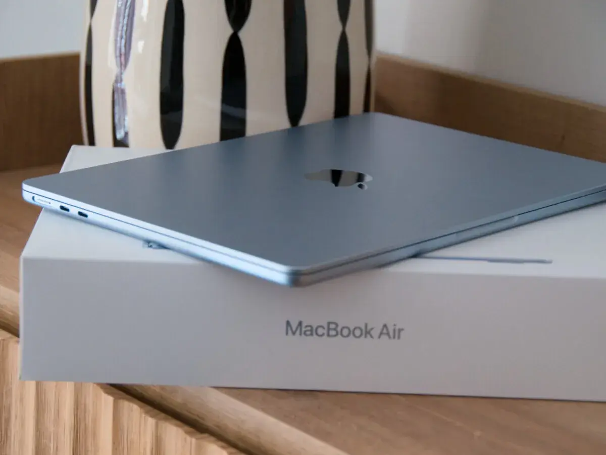 MacBook Air azul cerrado sobre su caja, con un jarrón al fondo.