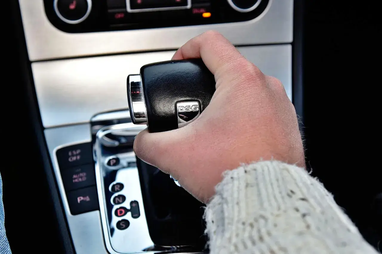 Dłoń trzymająca dźwignię zmiany biegów w samochodzie z napisem DSG. Widoczne przyciski ESP, Auto Hold i P.