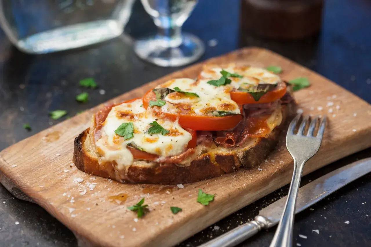 En härlig italiensk macka med smält ost, tomat och prosciutto på en träskärbräda.