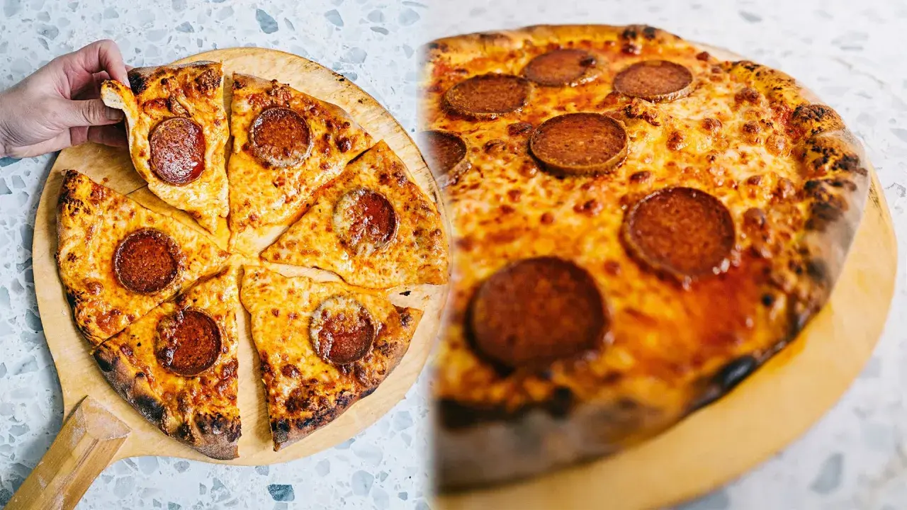 En hand tar en bit av en klassisk neapel pizza med pepperoni och smält ost.